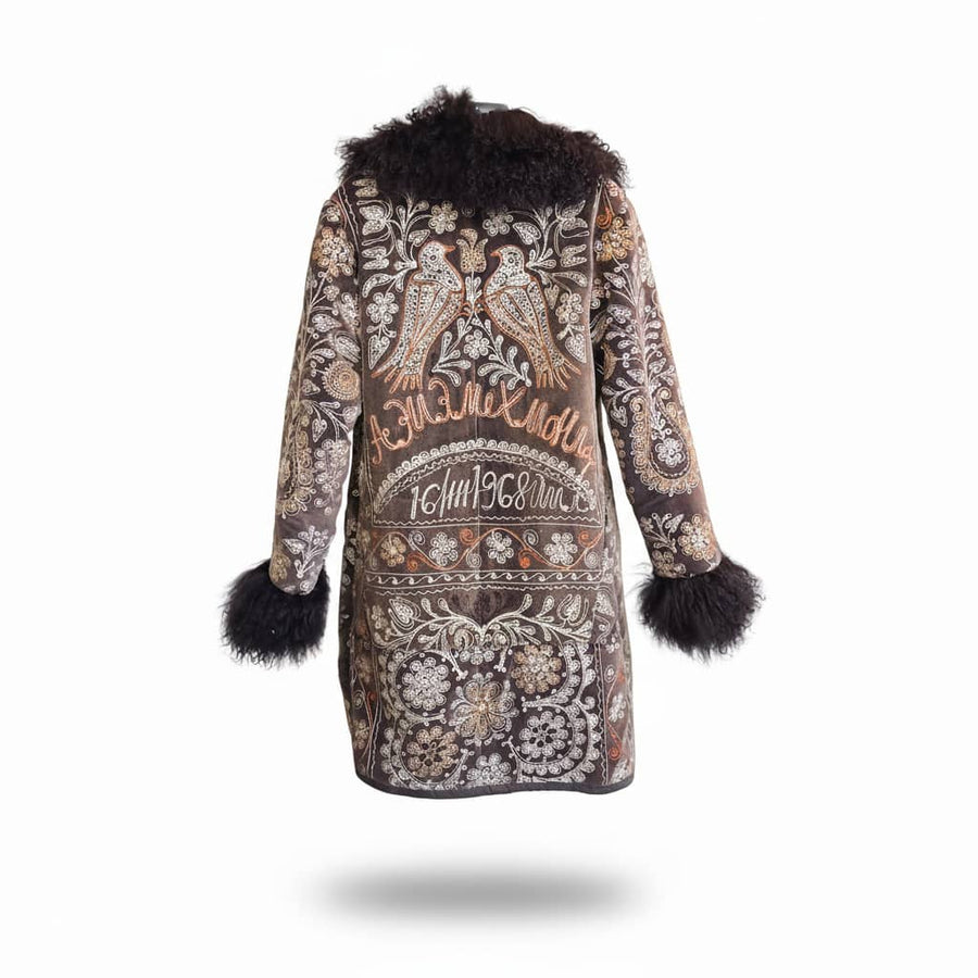 Back view of a black coat with intricate nightingale and floral embroidery and black curly fur collar and cuffs on a white background