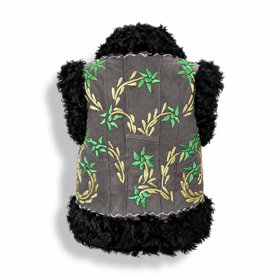 Back view of a charcoal grey suede vest with black curly shearling trim on the collar and hem, featuring gold and green embroidered floral vine patterns.