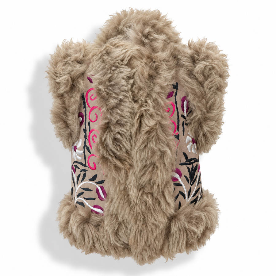 A fluffy faux-fur vest in a light tan/beige color, featuring embroidered floral and swirl patterns in pink, black, and white on the sides, shown against a plain white background.