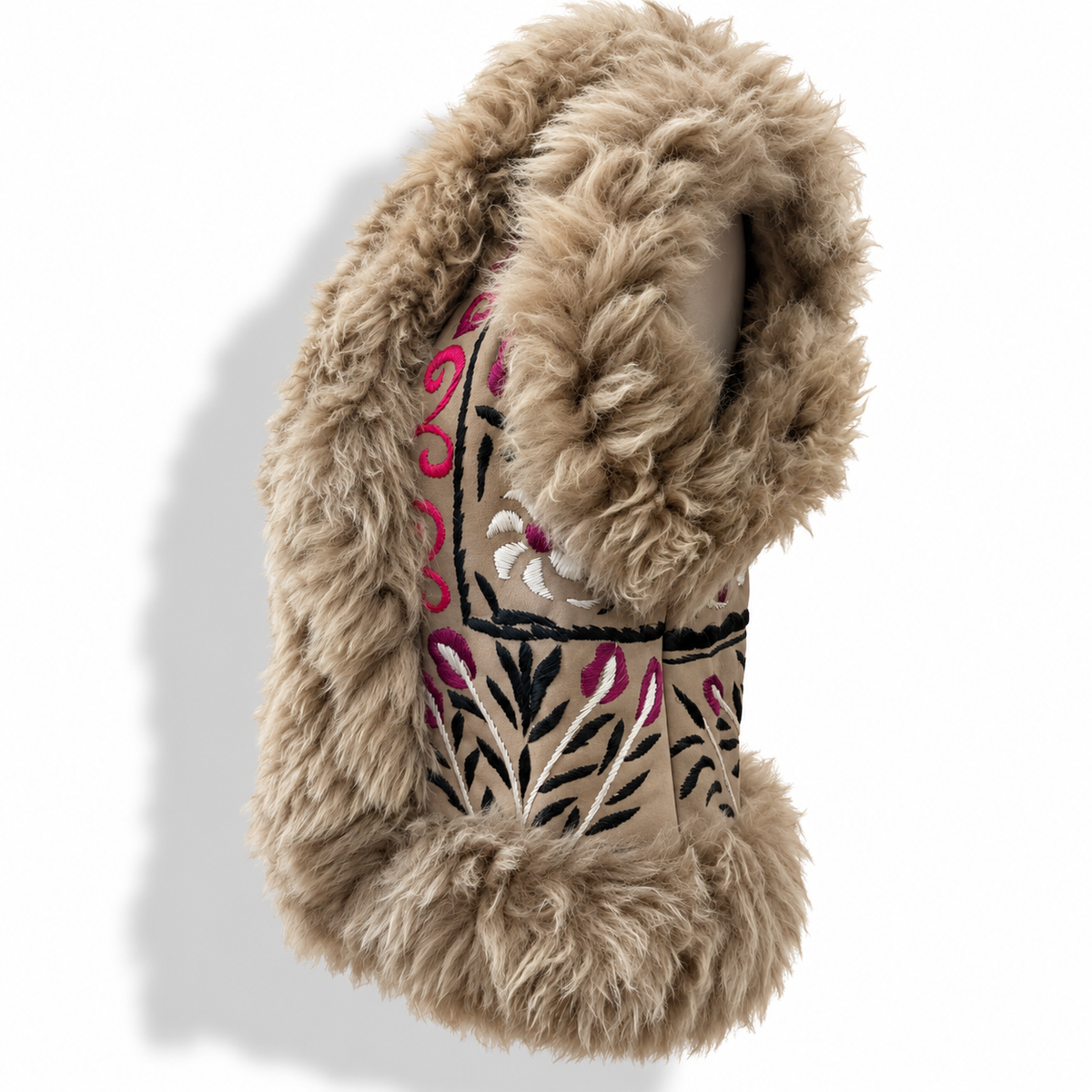Close-up side view of a tan shearling vest's shaggy fur hood and collar, with a central embroidered panel featuring pink, black, and white floral and leaf motifs.