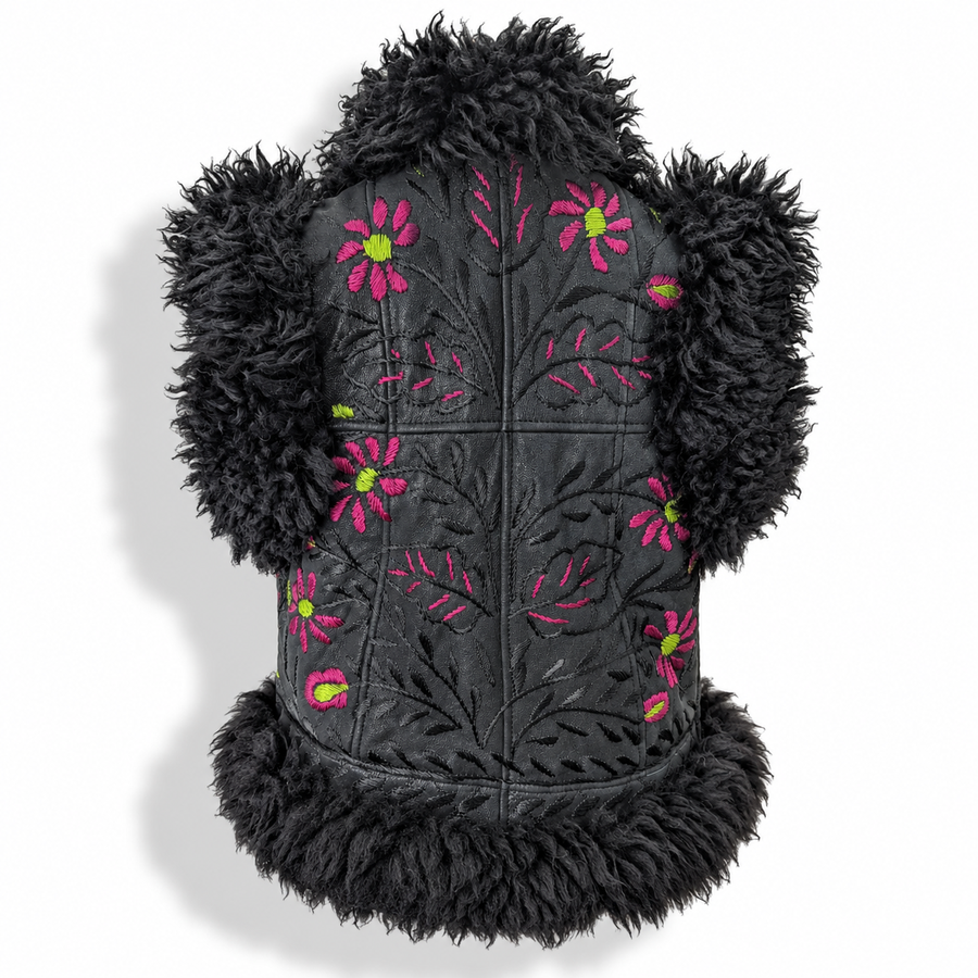 Back view of a black shaggy faux-fur vest with a black quilted center panel featuring pink and green embroidered flowers, displayed on a mannequin torso against a white background.