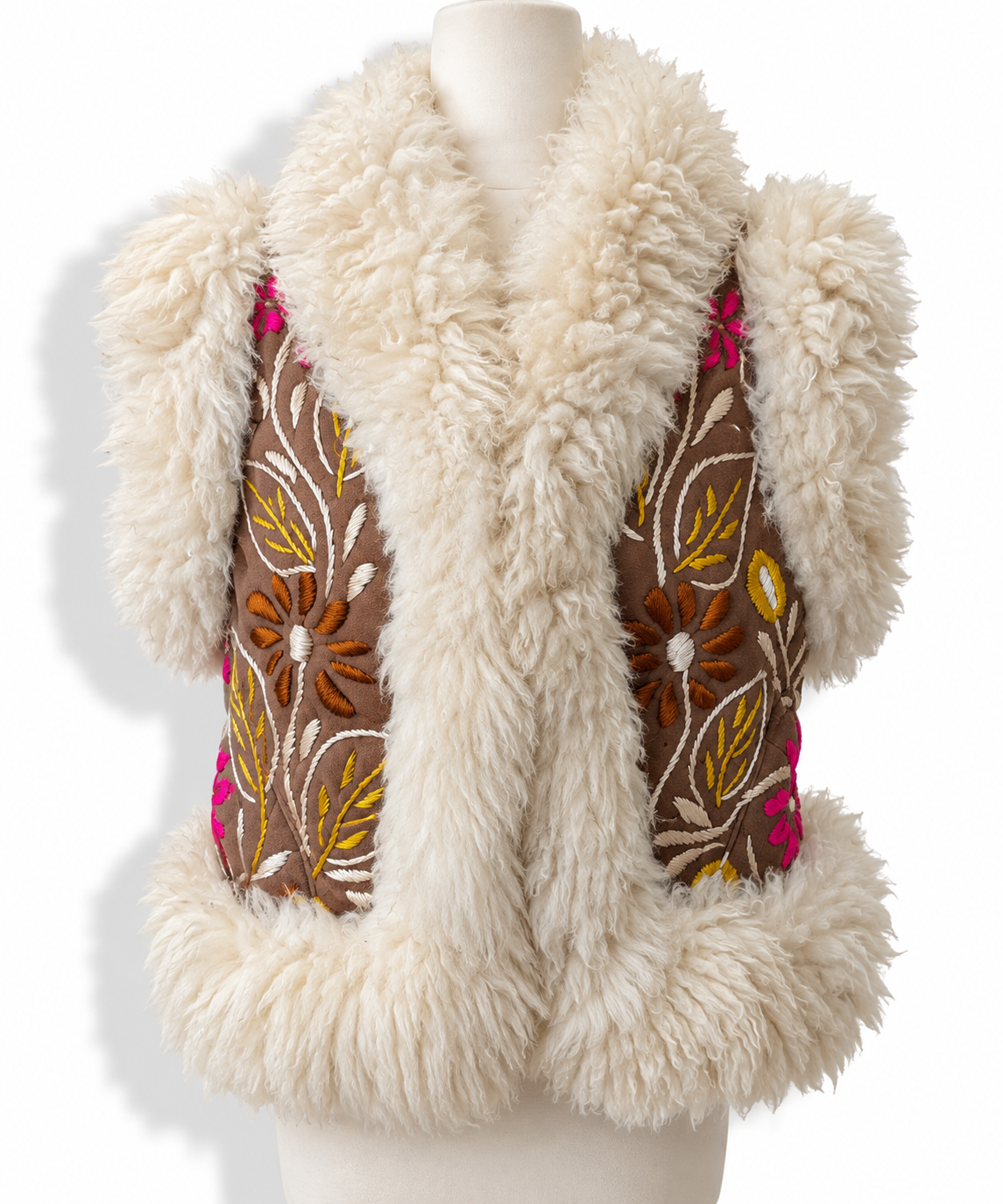 A cream-colored shearling vest with brown embroidered panels featuring floral and leaf patterns in yellow, orange, and pink, displayed on a mannequin torso against a white background.