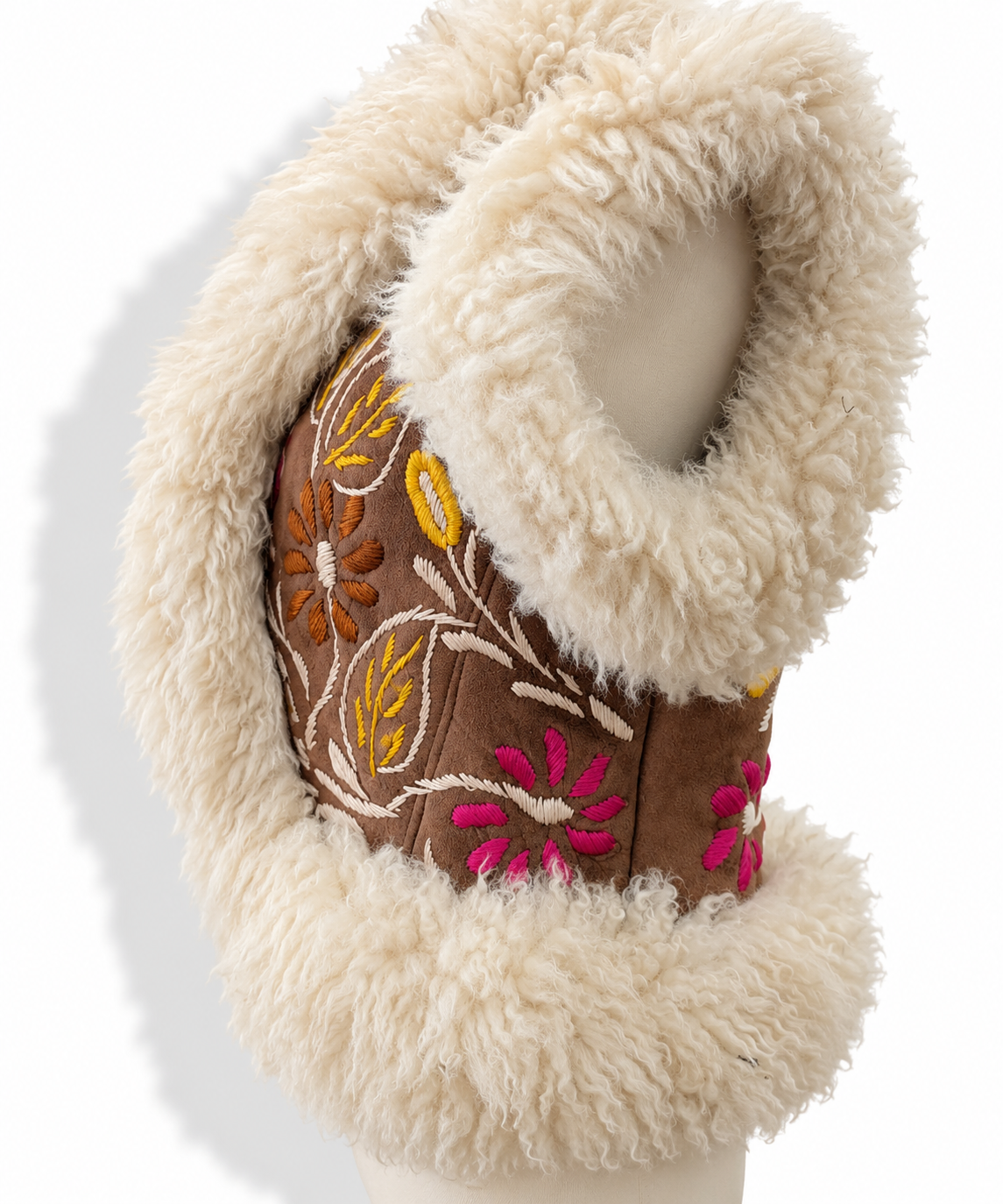 A close-up of a brown faux-leather vest or sleeve with a thick cream-colored faux fur trim and colorful floral embroidery in pink, yellow, and orange, displayed on a mannequin arm against a white background.