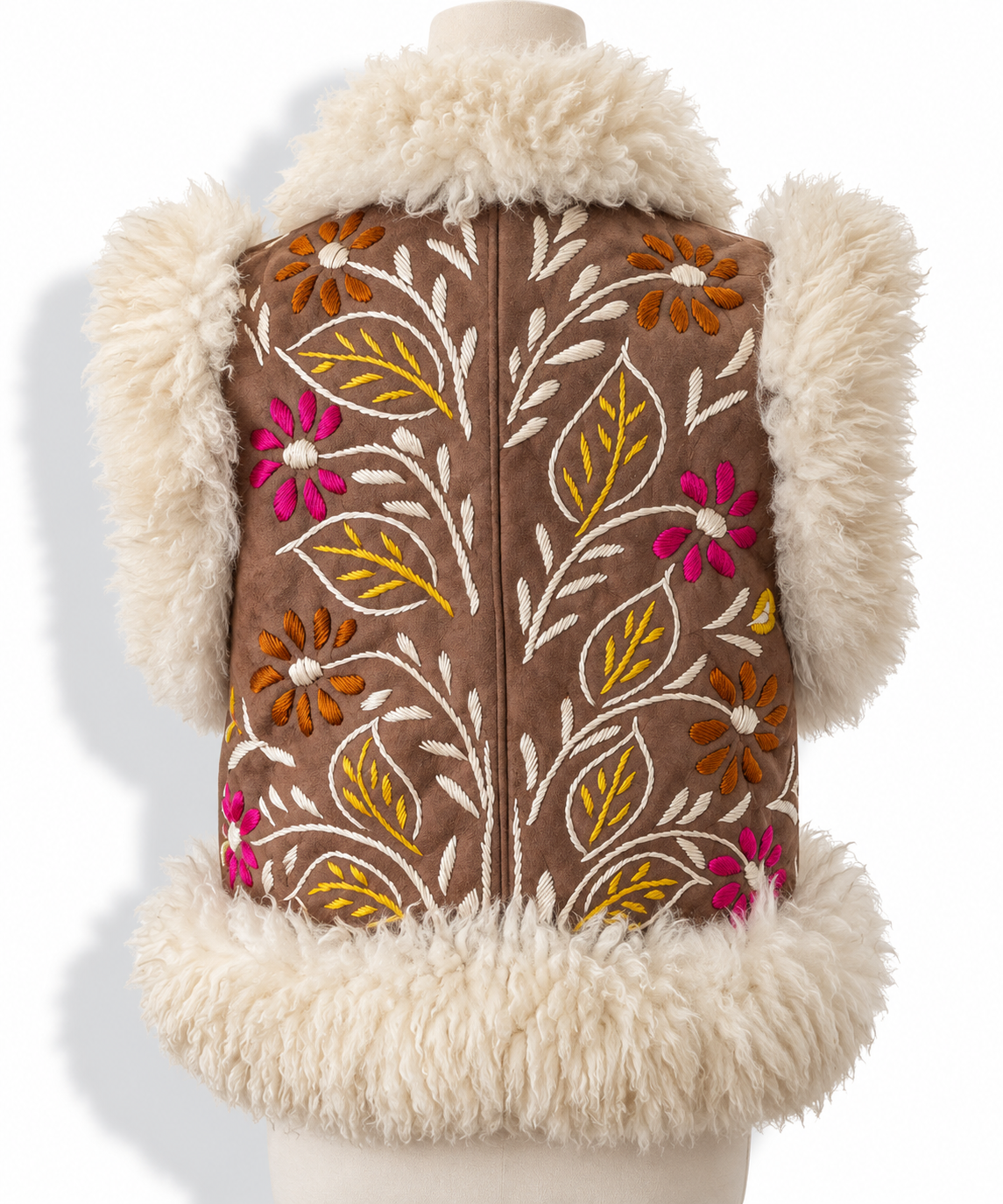 A brown suede vest with cream shearling trim and colorful floral embroidery, displayed on a mannequin against a white background.