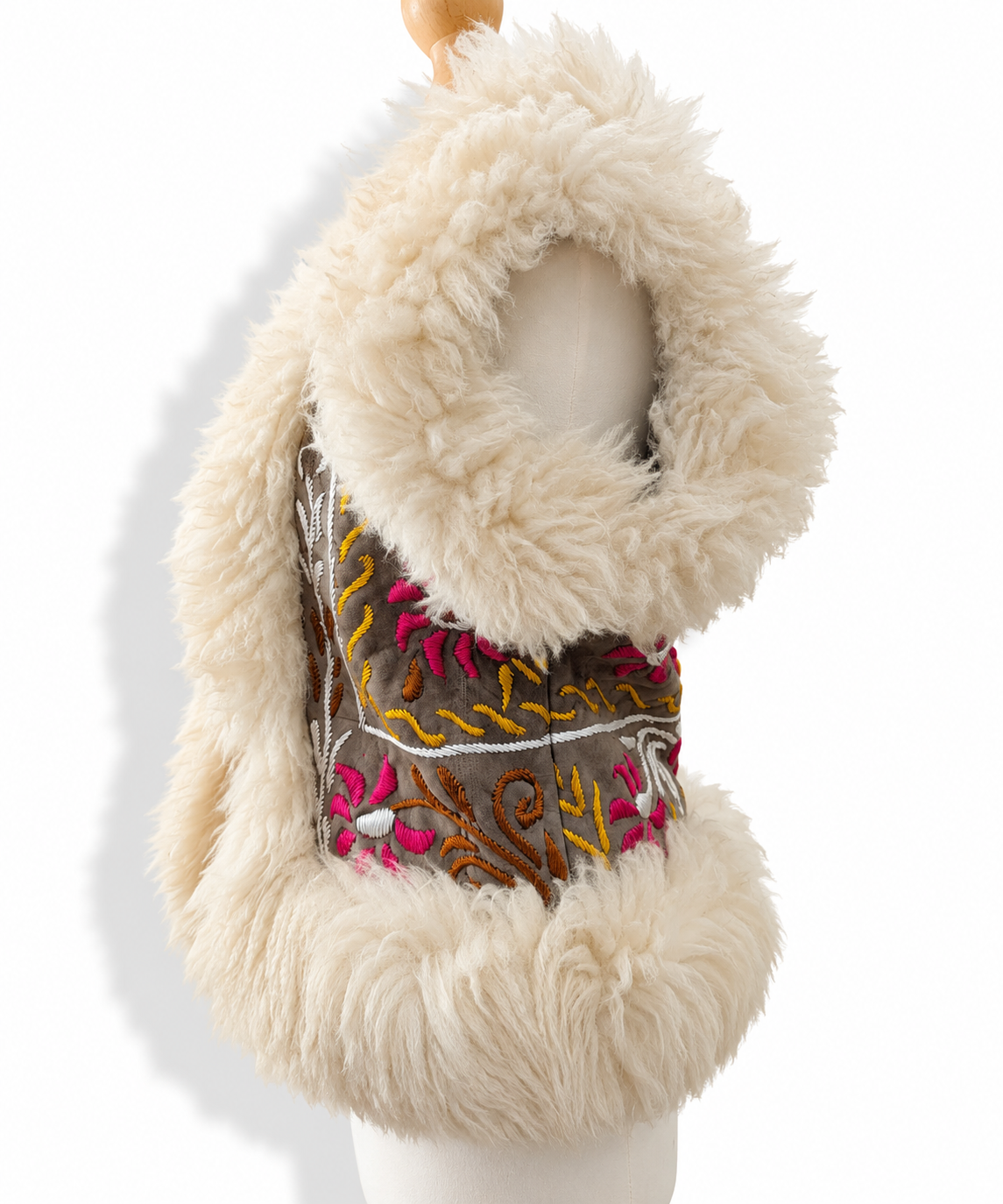 A cream-colored faux fur vest with a wide collar and a decorative embroidered chest panel, displayed on a white mannequin torso against a white background.