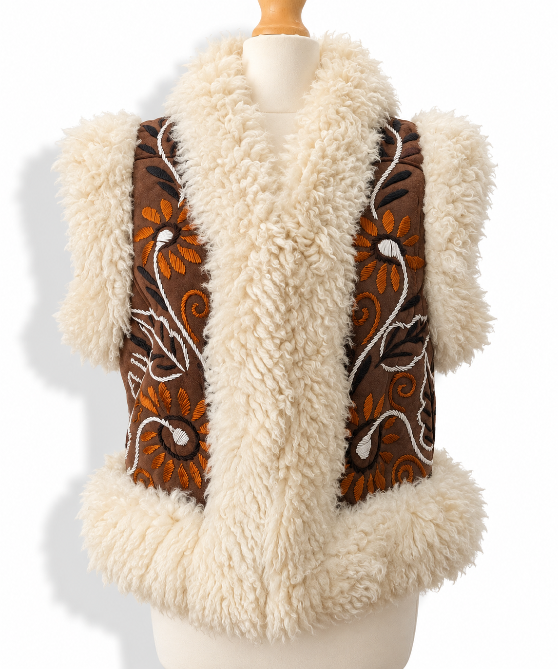 A cream-colored shearling vest with brown embroidered panels featuring orange and white floral patterns, displayed on a mannequin torso against a white background.