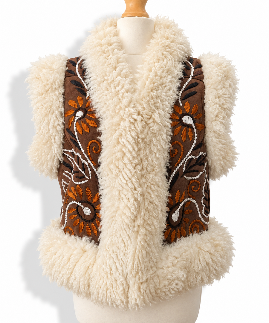 A cream-colored shearling vest with brown embroidered panels featuring orange and white floral patterns, displayed on a mannequin torso against a white background.