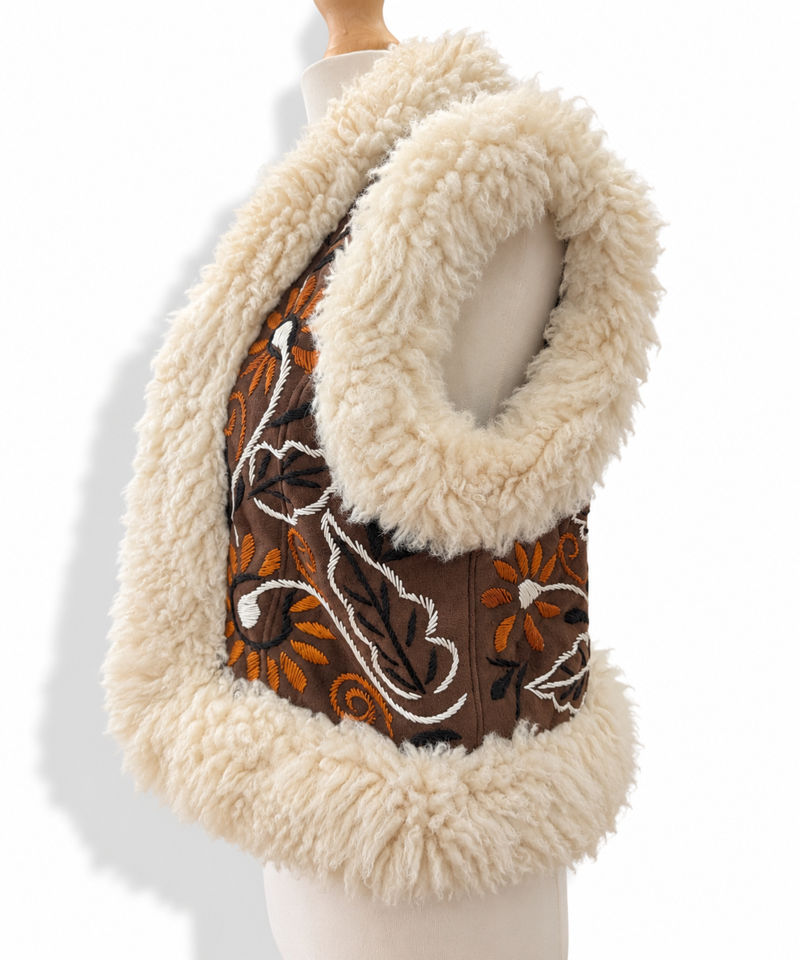 A sleeveless vest with a thick cream-colored faux fur trim and a brown center panel decorated with orange and white floral embroidery, displayed on a mannequin torso against a white background.