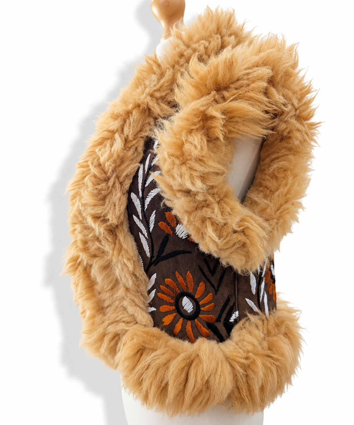 Side view of a brown vest with tan faux fur collar and trim, featuring an embroidered orange, white, and black floral panel, displayed on a mannequin torso against a white background.