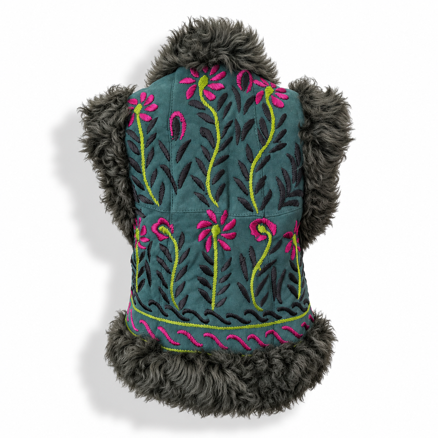 Back view of a teal suede vest with dark gray curly shearling trim, featuring pink and lime green floral embroidery, shown against a white background.