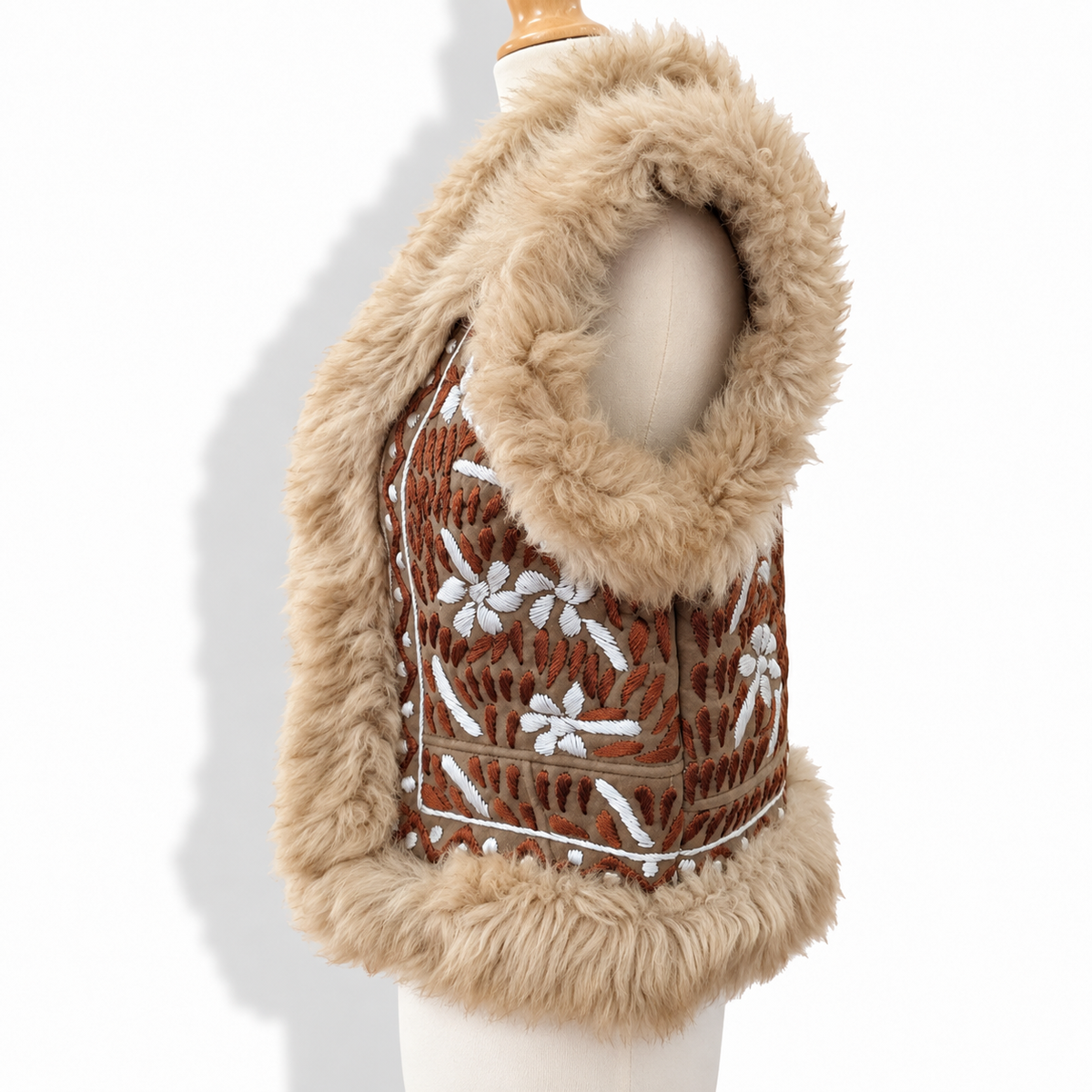 A sleeveless brown vest with a thick beige faux fur trim and white embroidered floral patterns, displayed on a cream mannequin torso against a white background.
