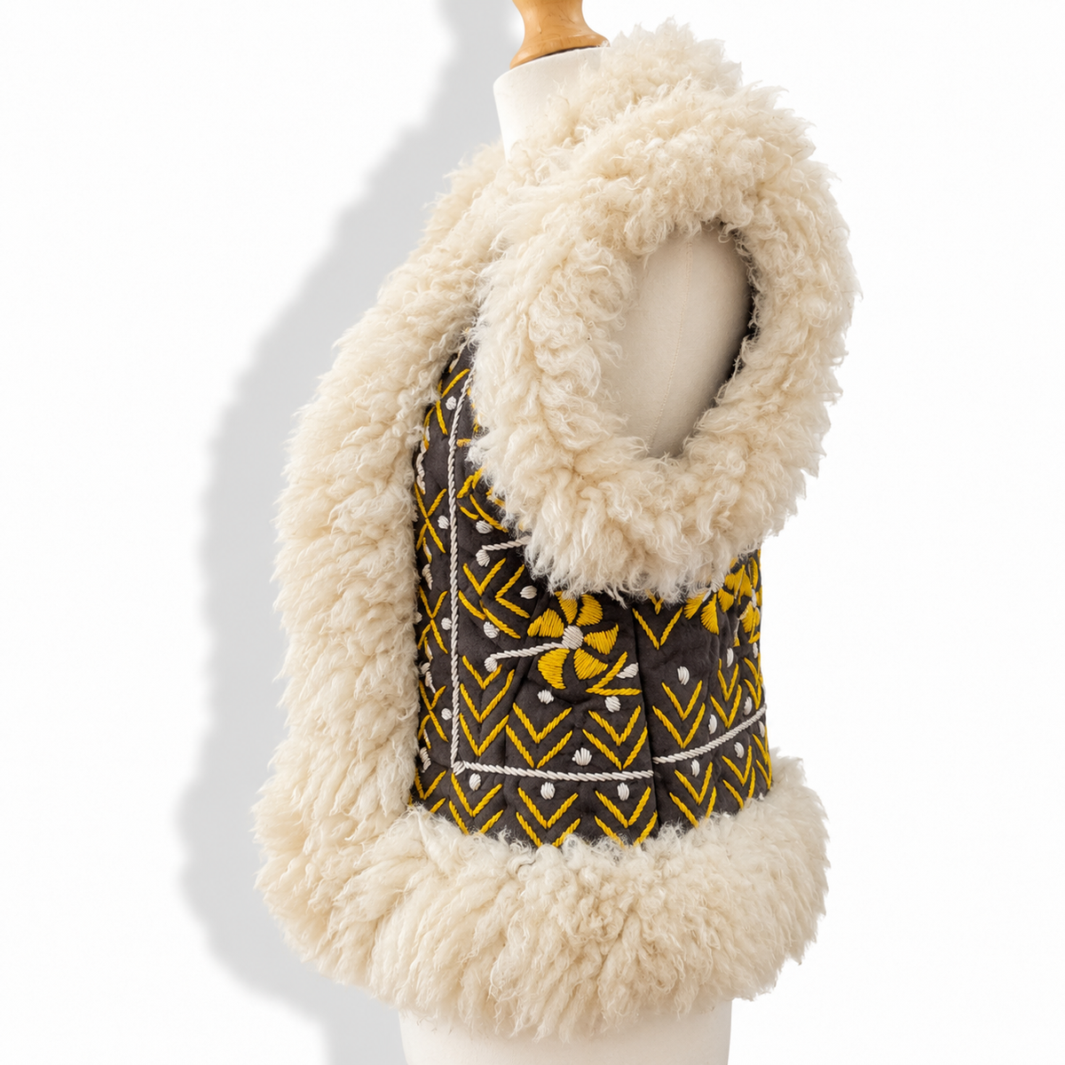 A sleeveless vest with a thick cream-colored curly faux-fur trim and a patterned center panel, displayed on a mannequin torso against a white background.