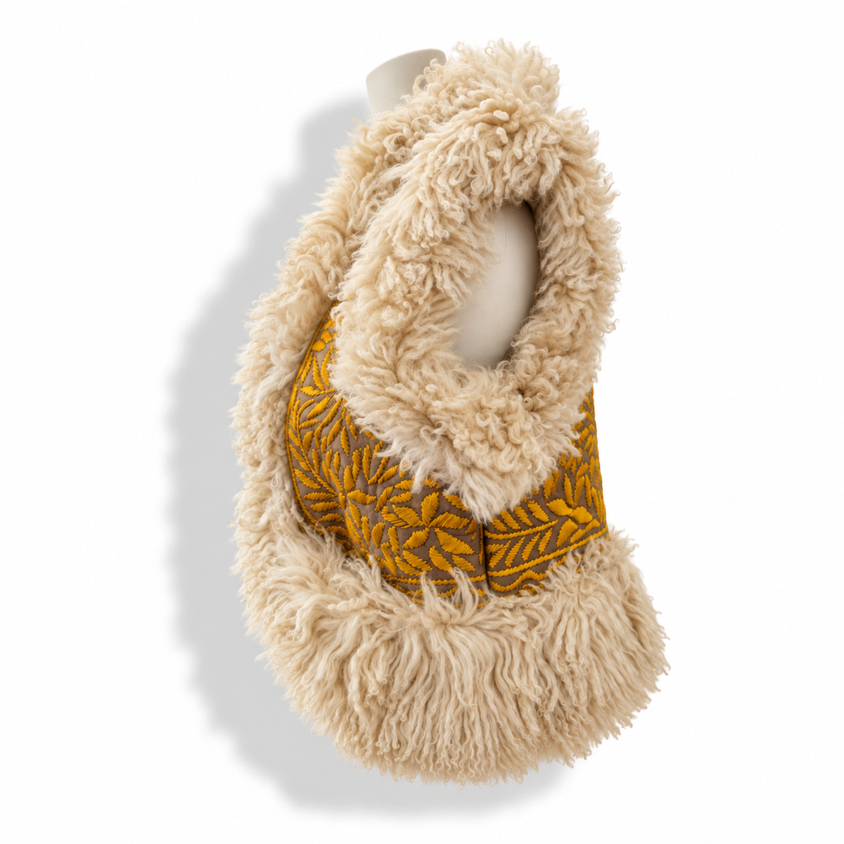 Side view of a vest with cream shaggy faux-fur collar and trim, featuring a tooled mustard and brown leaf-patterned leather panel, displayed on a mannequin torso against a white background.