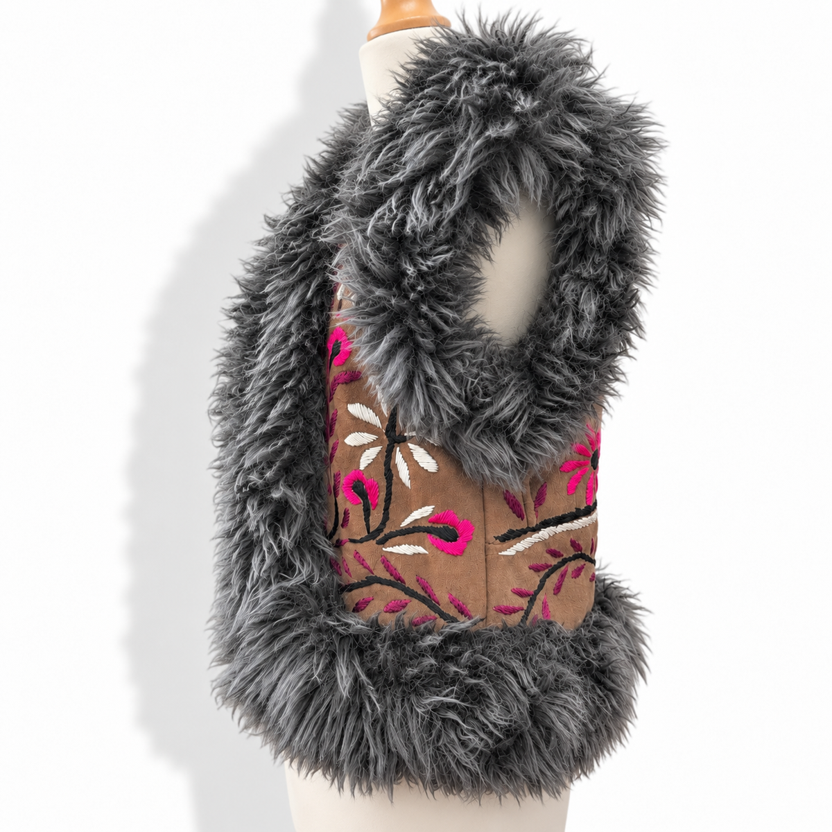 A sleeveless faux fur vest with a brown embroidered center panel featuring pink and white floral patterns, displayed on a cream dress form mannequin against a white background.