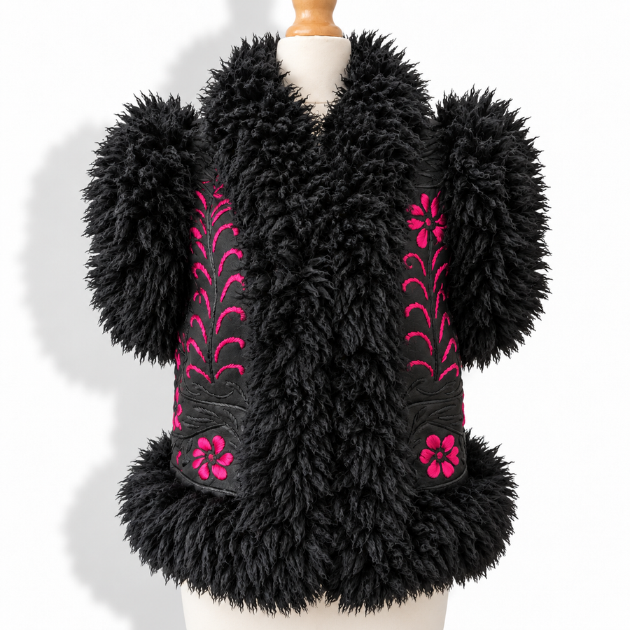 A black shaggy faux-fur vest displayed on a mannequin torso against a white background. The vest features bright pink embroidered floral and leaf patterns on the front panels and matching pink flower details near the lower front.