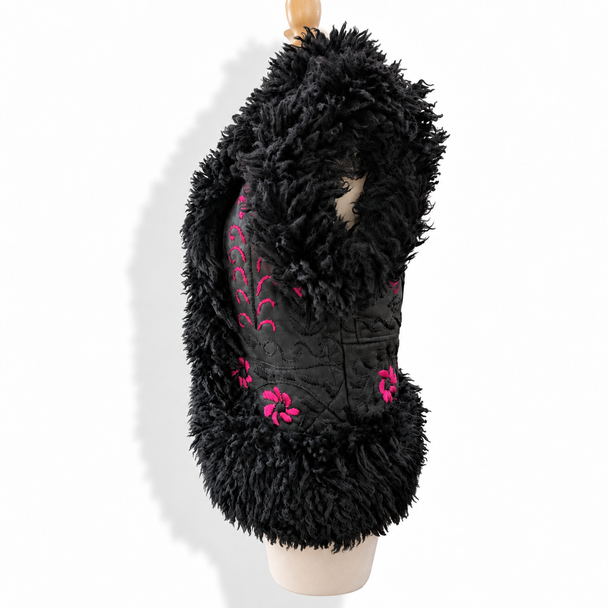 A black faux fur vest with pink floral embroidery and sequined detailing, displayed on a mannequin torso against a white background.