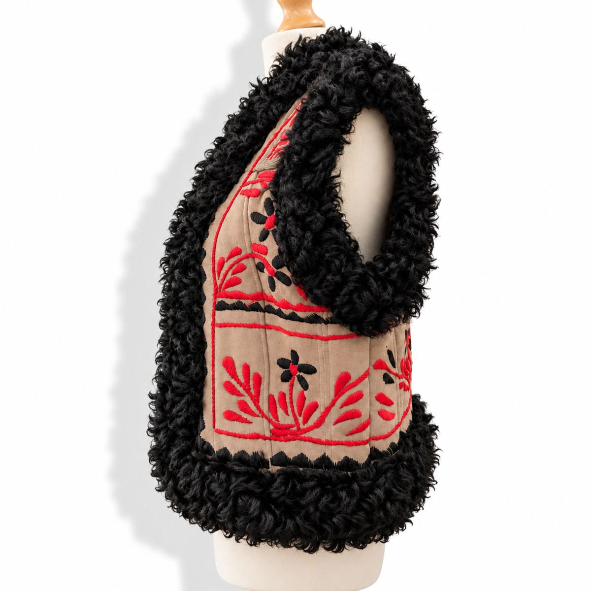 A sleeveless vest displayed on a cream dress form mannequin against a white background. The vest features a beige front panel with red and black embroidered floral patterns, framed by thick black curly faux-fur trim.