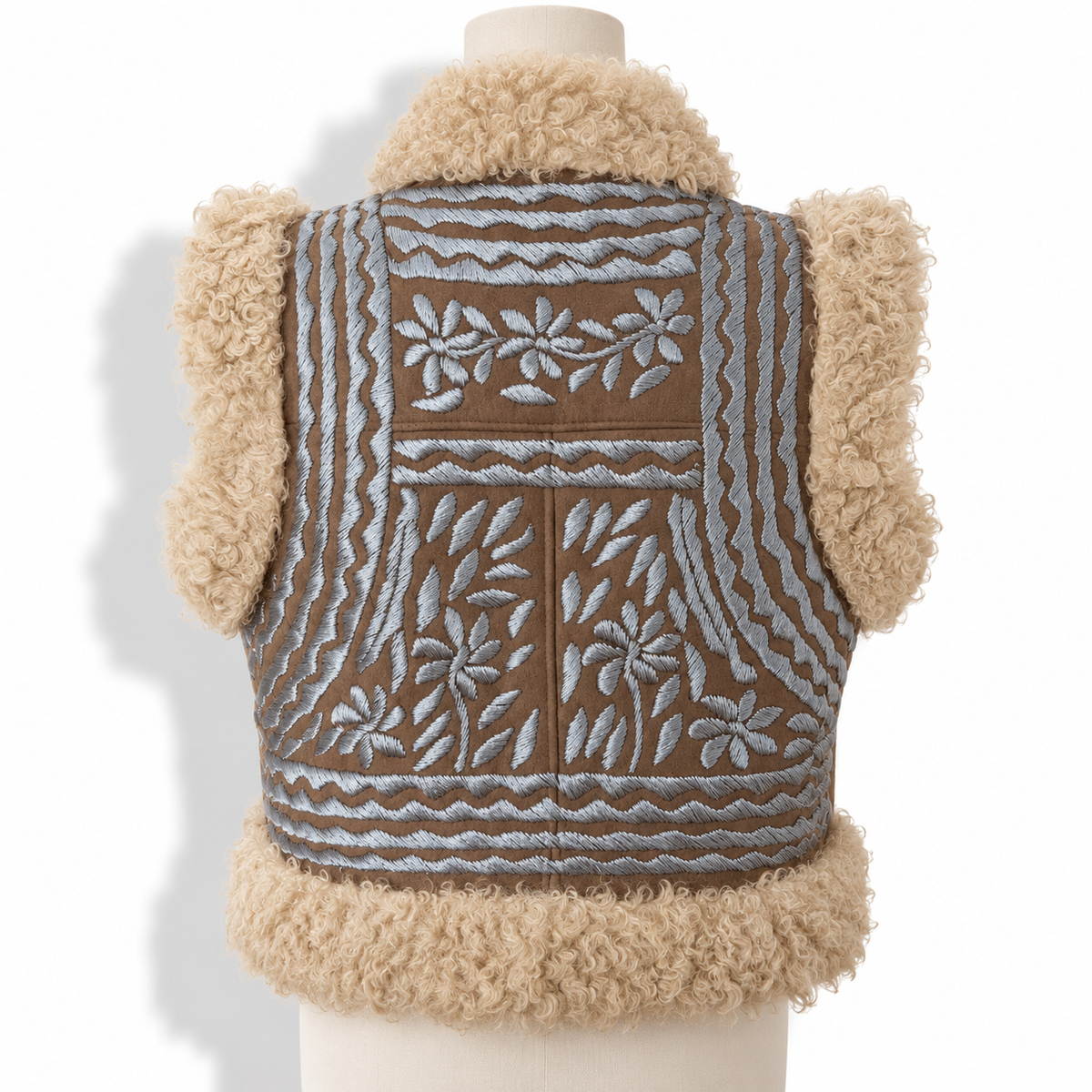A brown faux-leather vest with beige curly shearling trim on the collar, cuffs, and hem, featuring light blue-gray embroidered floral and geometric patterns on the front, displayed on a mannequin torso against a white background.