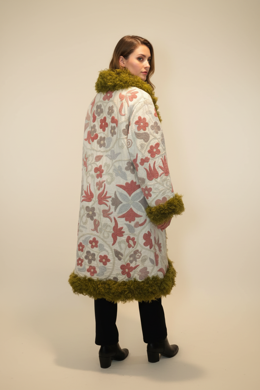 Woman seen from behind wearing a cream floral-patterned coat with olive green fur trim and black trousers, standing in a studio setting.
